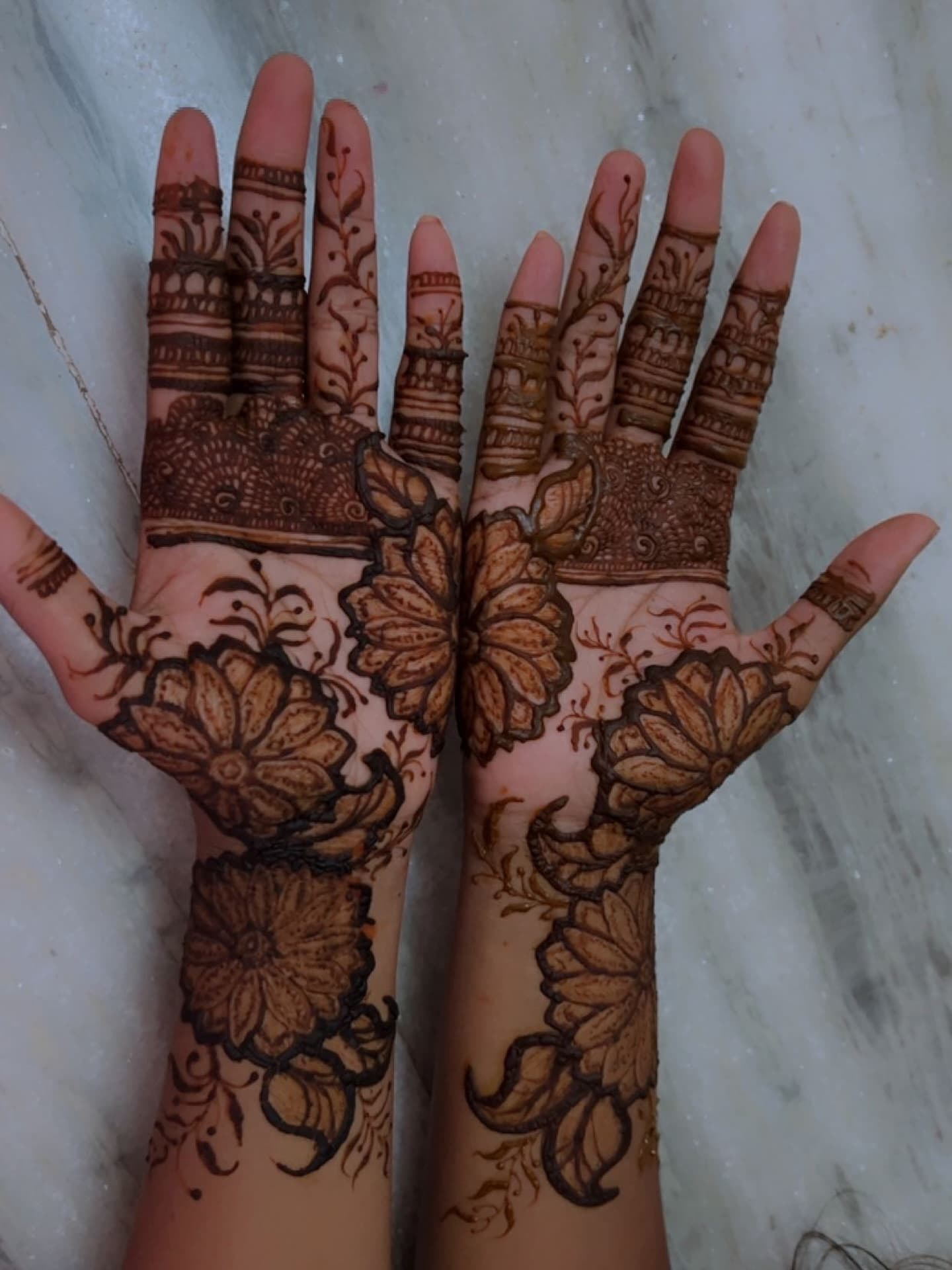 Two palms mirroring the same shell and floral henna pattern