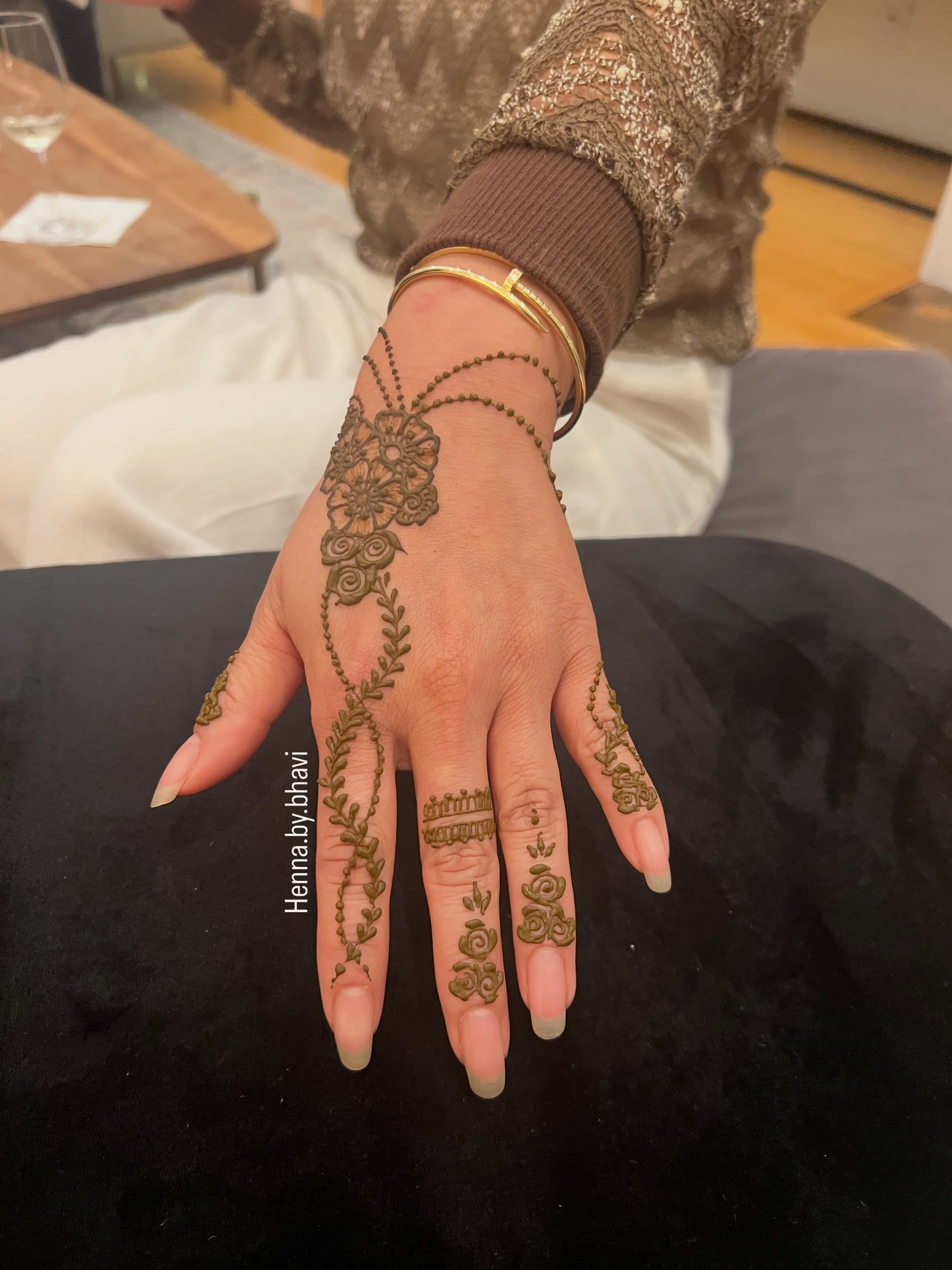A fine henna vine over the back of a hand stacked with gold bangles