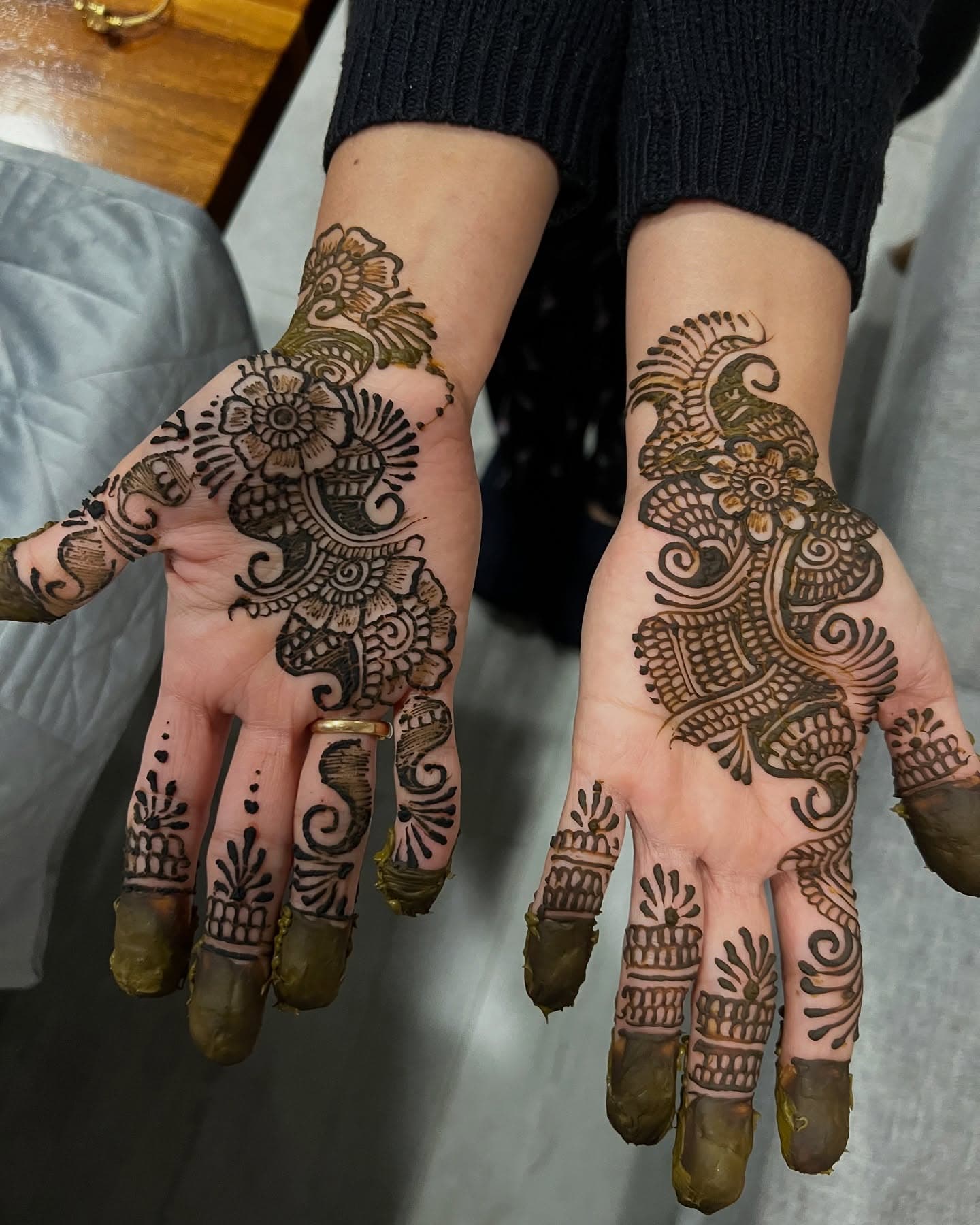 Two hands in full bridal henna with the paste still green on the fingertips